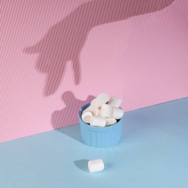 Creative layout of hands with shadow in the shape of a dog and a bowl of marshmallows on a blue-pink pastel background