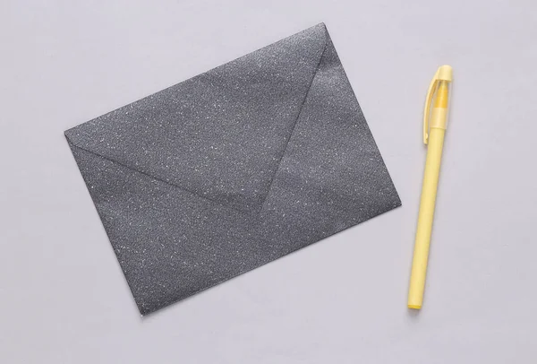 Black envelope with glitter and pen on gray background