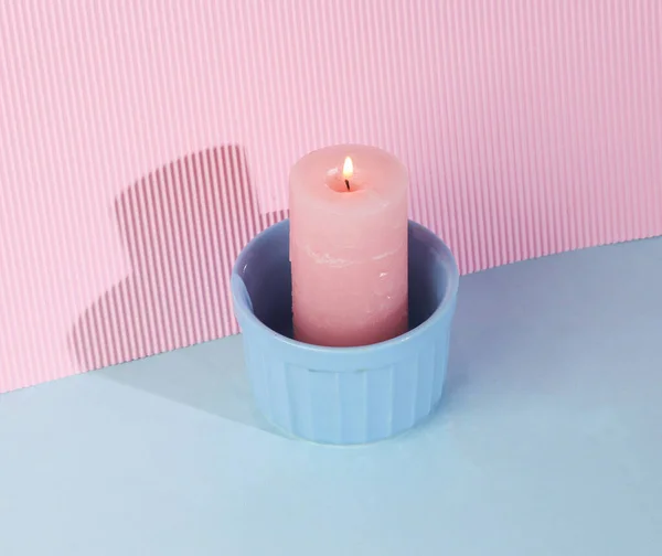 Flaming aroma candle in bowl on a blue-pink background with a shadow. Creative layout. Minimal composition