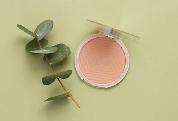 Powder box with a sprig of eucalyptus on a green background. Natural cosmetics concept