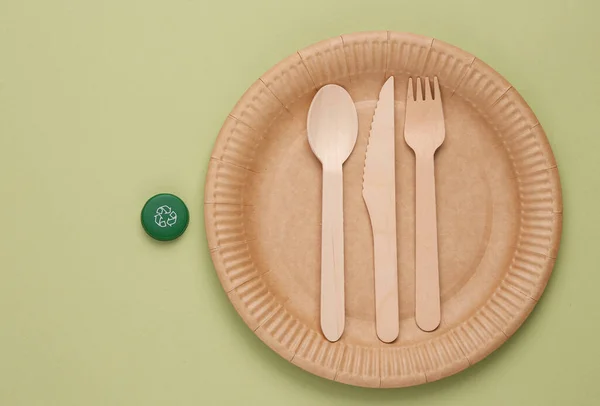 Eco products. No plastic. Zero waste. Plate with wooden fork, spoon and knife, Plastic bottle caps with circular recycling symbol  on green background. Natural materials. Top view