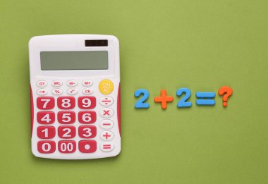 Calculator with an elementary equation on a green background. Mathematics, education, back to school. Top view