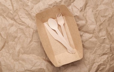 Set of wooden fork, spoon and knife in plate on crumpled craft paper background. Zero waste simple creative concept. Trendy wooden eco things. Top view, Flat lay
