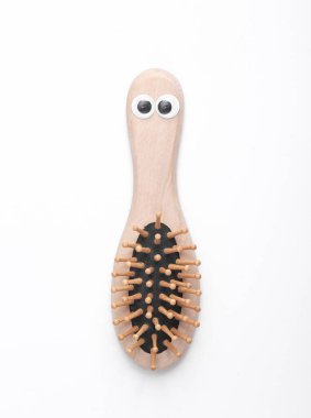 Wooden hair brush with eyes on white background. Eco concept