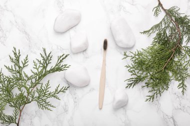 Eco toothbrush with white pebble stones and sprigs of fir on a marble background. Natural composition. Dental care. Top view