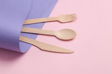 Wooden knife, spoon and fork on purple pink background. Eco products