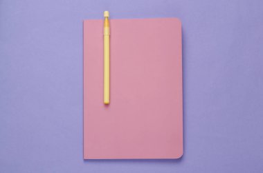 Pink notepad with pen on purple background
