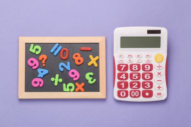 Education concept. Maths. Calculator and chalk board with plastic magnetic numbers on purple background