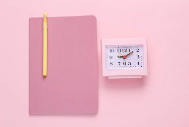 Pink notebook with a clock on a pink background. Flat composition