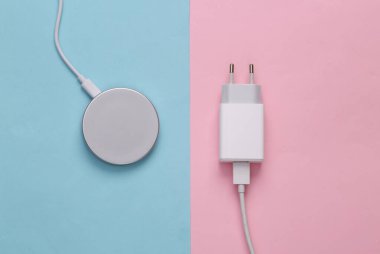 The evolution of gadgets. Wireless charging platform and wired charging adapter on a pink-blue background. Top view