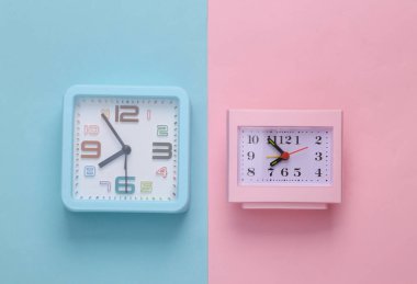 Two table clocks on a blue-pink pastel background.Top view