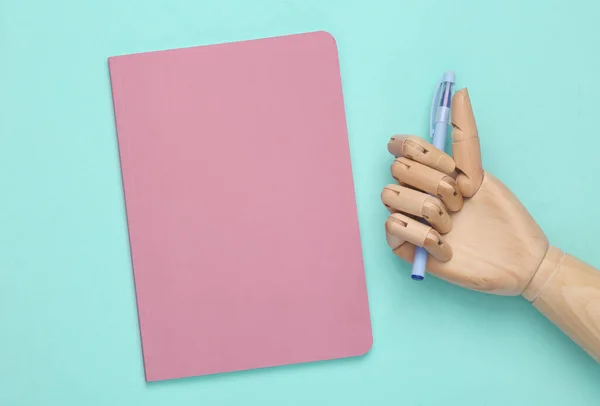 Pink blank notepad cover and wooden hand with pen on blue background