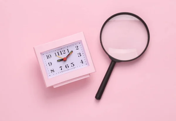 Clock with a magnifying glass on pink background. Top view