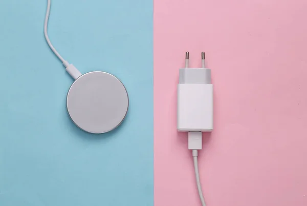 The evolution of gadgets. Wireless charging platform and wired charging adapter on a pink-blue background. Top view