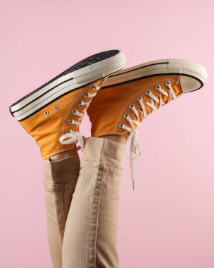 Pembe arka planda, 80 'lerin modası geçmiş sarı spor ayakkabılı kadın bacakları.