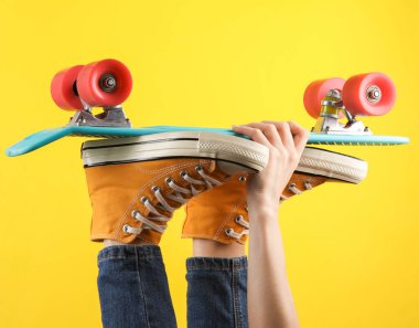 80 'lerin kadın bacakları, sarı spor ayakkabılar ve panoda kot pantolon, sarı arka plan.