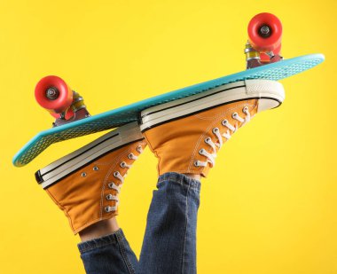 80 'lerin kadın bacakları, sarı spor ayakkabılar ve panoda kot pantolon, sarı arka plan.