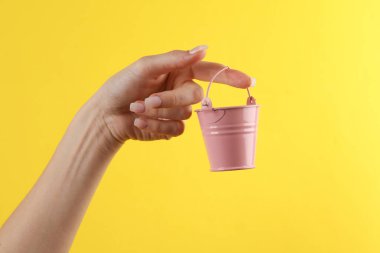 Kadının eli sarı arka planda mini bir kova tutuyor.