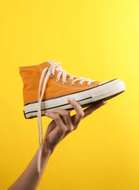Kadının eli, sarı arka planda 80 'lerin sarı lastik ayakkabısını tutuyor.