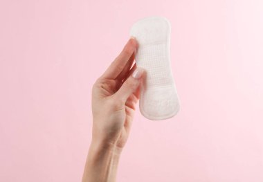 Kadının eli pembe arka planda pedi tutuyor. Kadın hijyeni, adet görme, kritik günler.