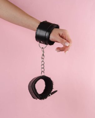 Pembe arka planda deri kelepçeli kadın eli. BDSM aksesuarlar, hakimiyet, seks oyunları