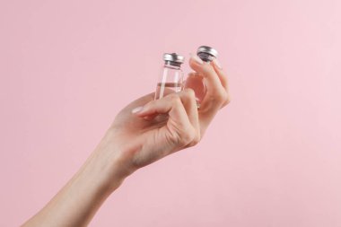 Aşı şişeleri pembe arka planda bir kadının elinde