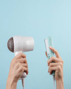 Saç stili. Mavi arka planda kadın eli ütülü saç kurutma makinesi. Güzellik ve moda