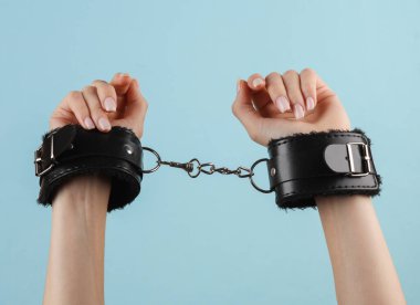 Mavi arka planda deri kelepçeli kadın elleri. BDSM aksesuarlar, hakimiyet, seks oyunları