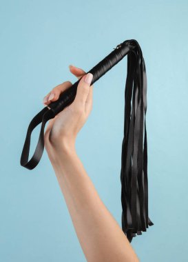 Mavi arka planda deri kamçı tutan kadın eller. BDSM aksesuarlar, hakimiyet, seks oyunları
