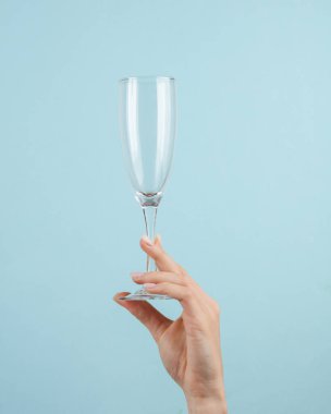 Mavi arka planda bir kadının elinde boş şampanya bardağı.