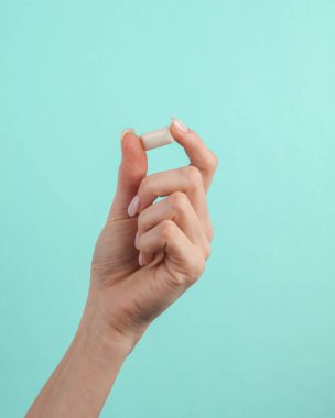 Mavi arka planda beyaz hap ve kadın eli. Tıp konsepti