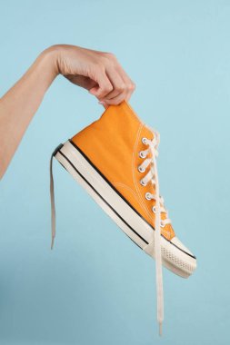 Sarı retro ayakkabılı, mavi arka planda bir kadın eli.