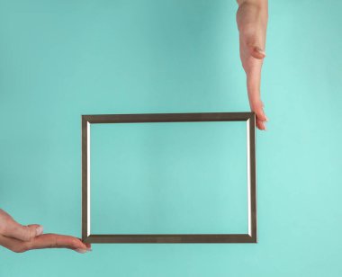 Mavi arka planda altın rengi boş bir çerçeve tutan bir kadının elleri