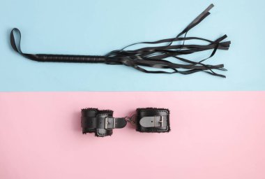 Mavi-pembe pastel arka planda kelepçeli deri kamçı. Seks oyunları, hakimiyet, bdsm