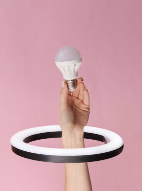 Kadının eli, pembe arka planda, kurşunlu halka lambasının içinden ampulü tutuyor. Yaratıcı fikir.