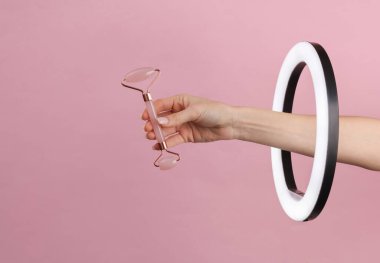 Kadının eli yeşil yüz masajı silindirini pembe arka plandaki kurşun halkalı lambanın içinden tutuyor. Yaratıcı bir fikir. Güzellik konsepti