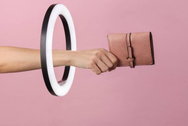 Kadının eli, pembe arka plandaki kurşun halkalı lambanın içinden deri çantayı tutuyor. Yaratıcı bir fikir. Moda konsepti