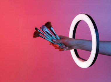 Makyaj fırçalarını kırmızı neon ışıklı lamba içinde tutan bir kadın. Yaratıcı bir fikir. Güzellik günlüğü