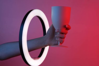 Kadının eli, kırmızı mavi neon eğimli ışıkta, kurşun halkalı lambanın içinden plastik cam tutuyor. Yaratıcı fikir.