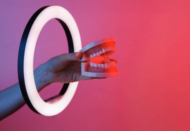 Kadının eli insan çene modelini kırmızı neon ışık altında kurşun halka lambasının içinden tutuyor. Yaratıcı bir fikir. Diş bakımı