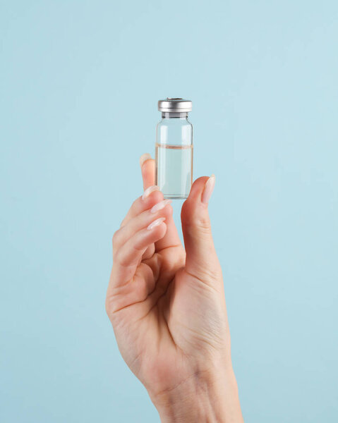 Vaccine bottles in a female hand on a blue background
