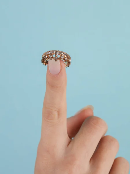 Golden ring in the form of crown with diamonds on female finger. Blue background