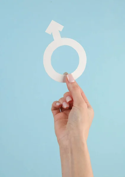 在蓝色背景下 女性的手拿着男性的性别符号 — 图库照片