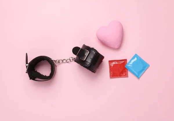 stock image Handcuffs from a sex shop with condom pack and a heart on a pink background. Sex games