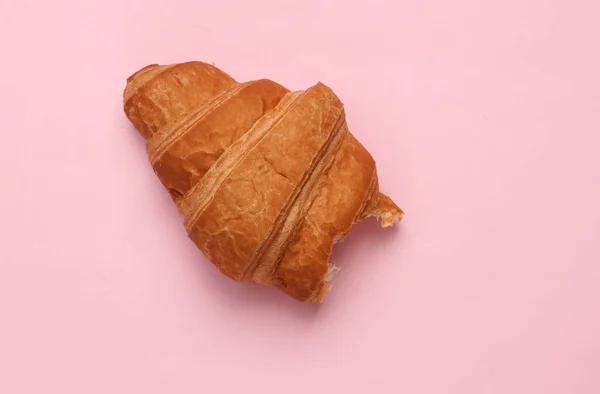 Appetizing bitten croissant on a pink background