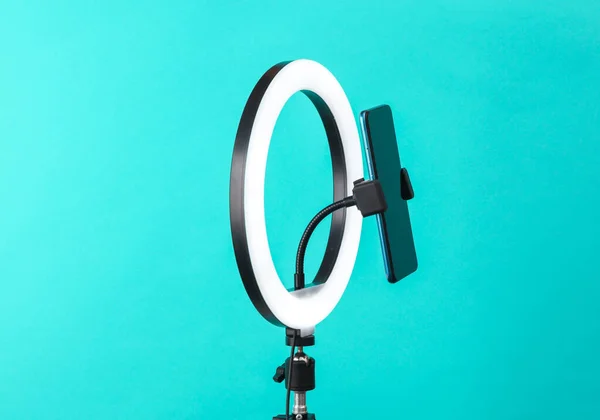 Led ring lamp with smartphone on tripod, blue background. Vlogging, beauty blog