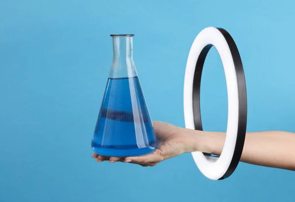 青色の背景にLedリングランプを通して女性の手を保持実験室のフラスコ 創造的なアイデア — ストック写真