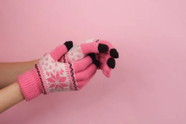 Women\'s hands in warm knitted gloves with a pattern on a pink background