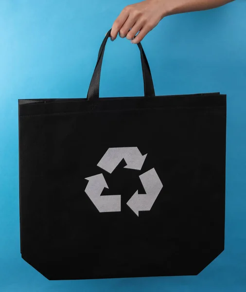 女用手拿着蓝色背景的圆形回收利用标志的黑色购物袋 — 图库照片