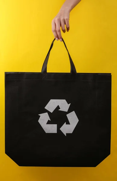 女用手提着黑色购物袋 黄色背景上有圆形回收标志 — 图库照片